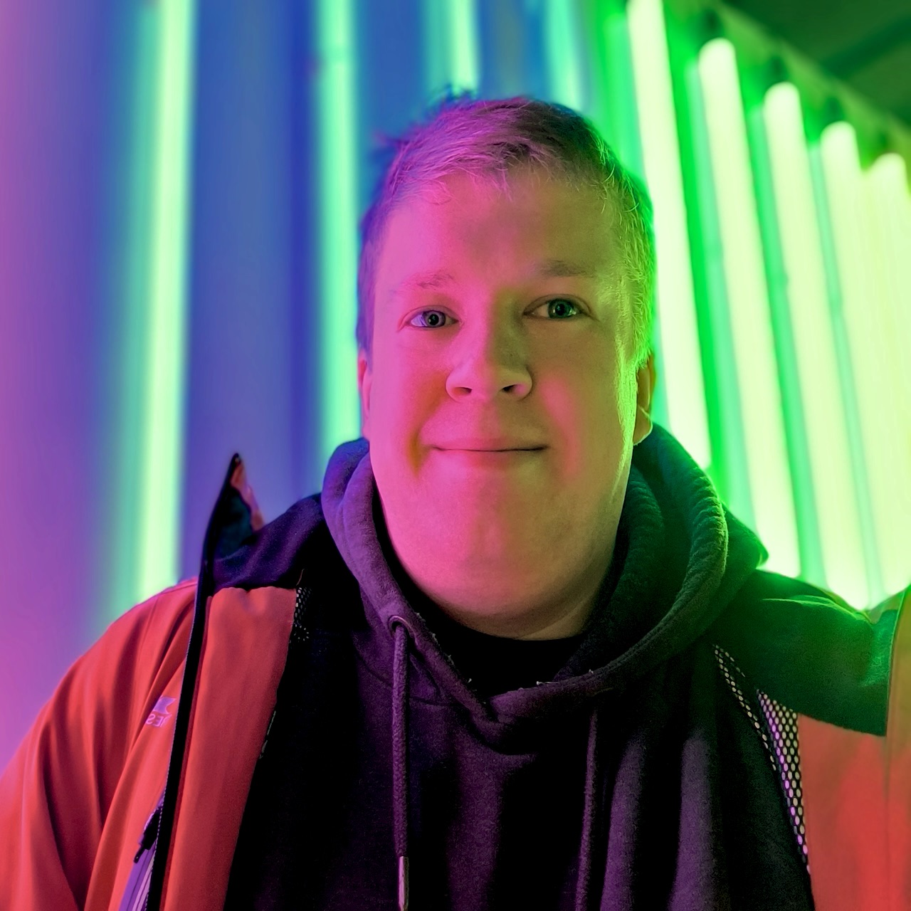 A photo of Matthew Stratford behind bright strips of rainbow light.